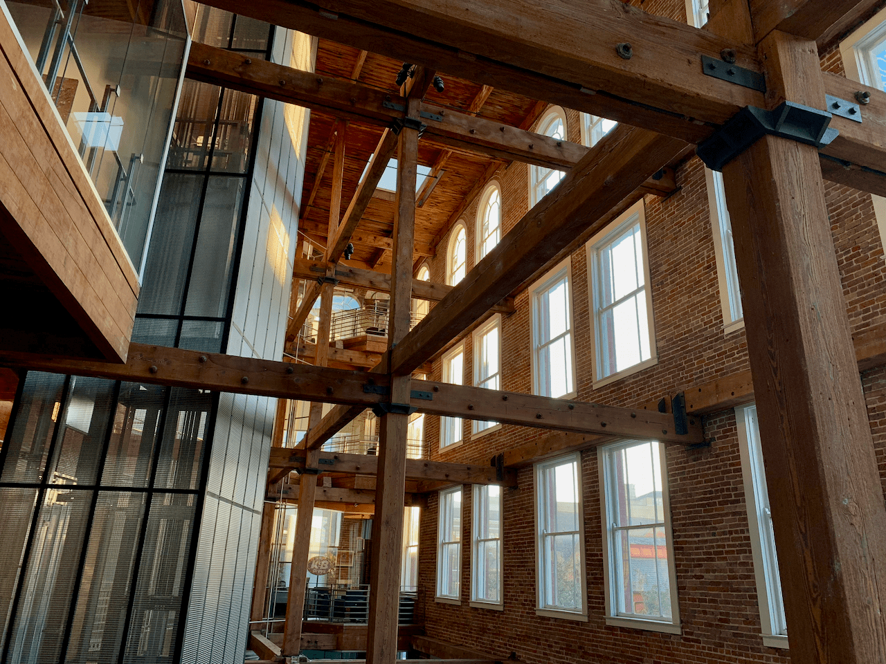 Interior of a renovated building with exposed timber beams, brick walls, and large windows